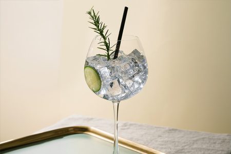 Gin and Tonic cocktail viinilasissa tarjottimen päällä kurkkuviipaleella ja rosmariinin oksalla koristeltuna