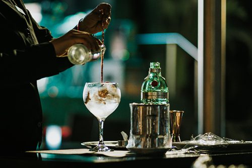 Gin and Tonic cocktail, jota valmistellaan baarissa. Juomaa sekoitetaan baarilusikalla samalla kun juomaan kaadetaan tonic vettä